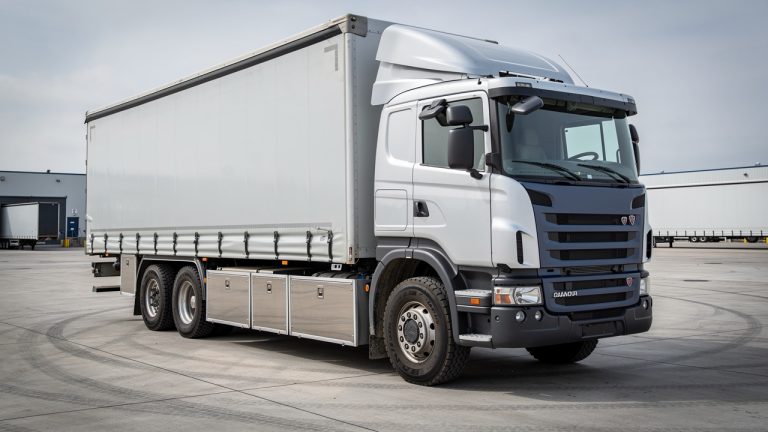 Camion poids lourd stationné dans un dépôt professionnel, avec un coffre de rangement fermé sous le châssis, photographié en lumière naturelle.