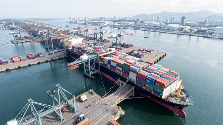 Vue aérienne réaliste d’un grand port taïwanais moderne, avec un porte-conteneurs à quai relié à l’électricité et des portiques automatisés dans un environnement industriel propre.